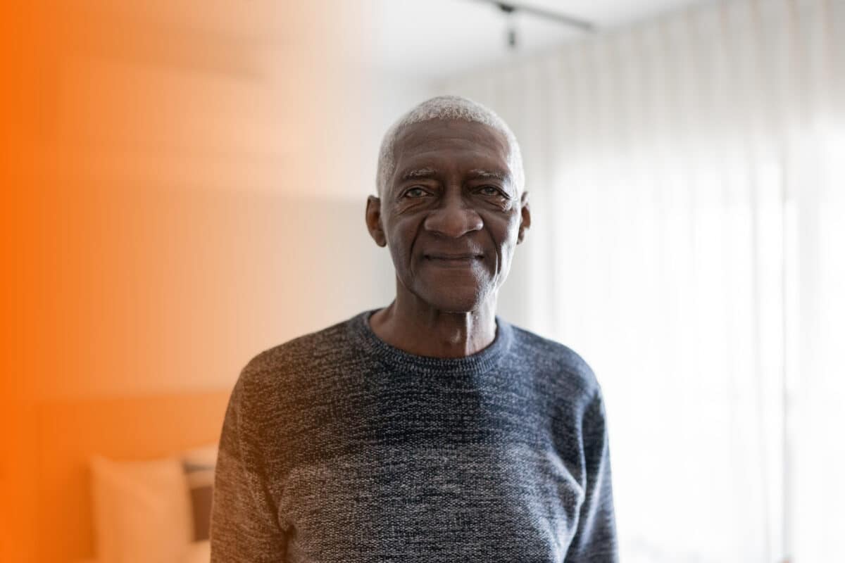 Older man standing in his own bedroom.